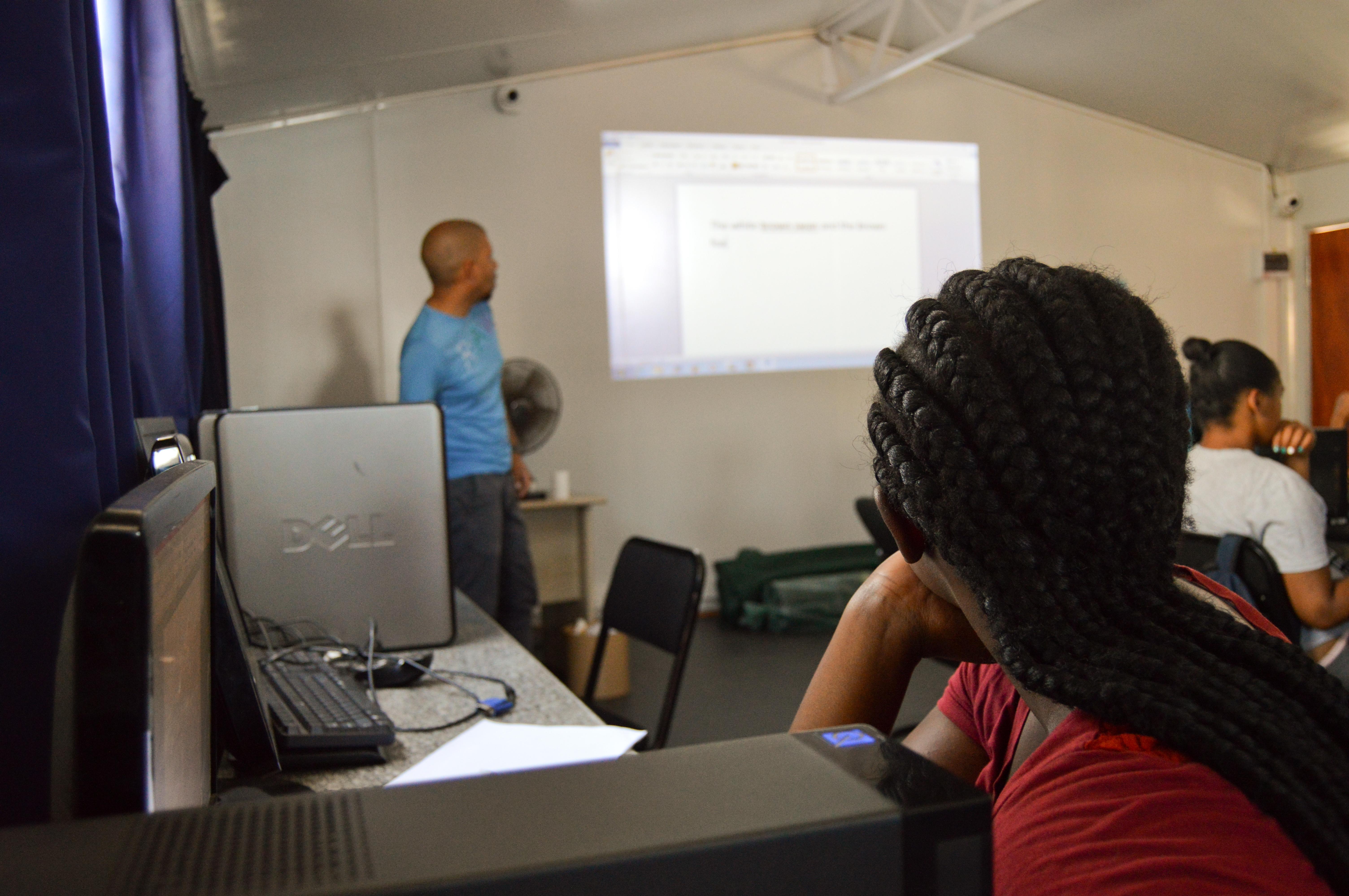 Voluntario profesor de informática en Sudáfrica durante una de sus clases. Estudiante recibiendo una clase de informática de nuestro voluntario en Sudáfrica.